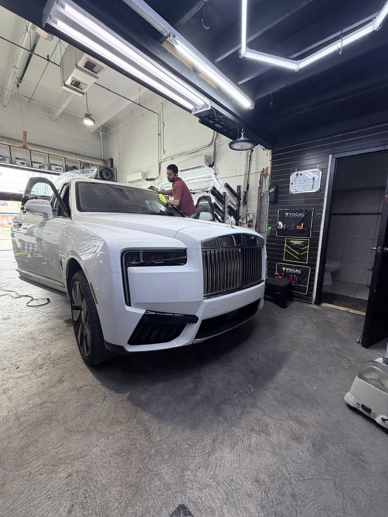 White luxury SUV inside the workshop bay under overhead lighting while a technician works nearby.